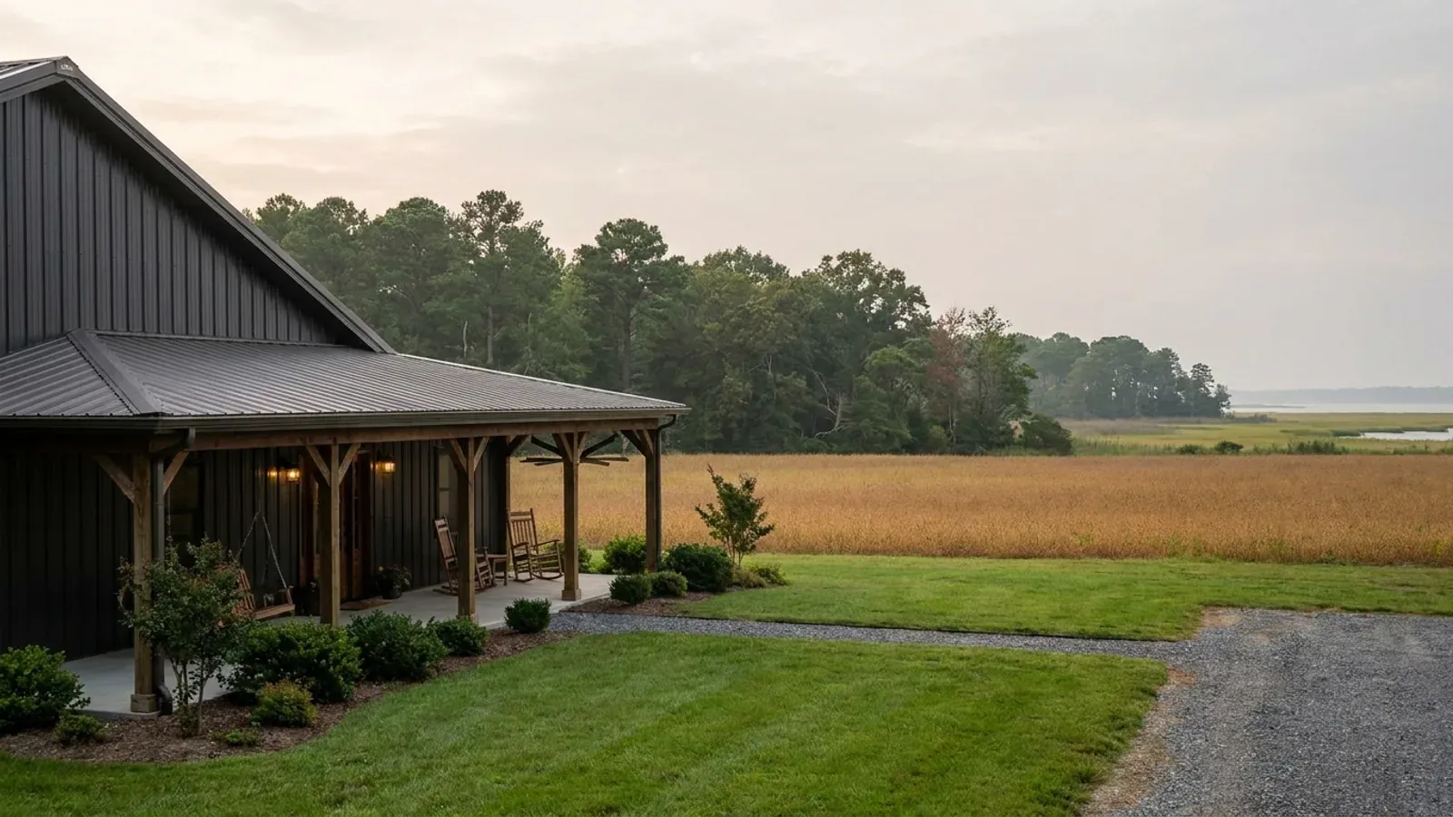 A barndominium exterior showing a deep wrap-around covered porch with posts and railing along two sides of the building.