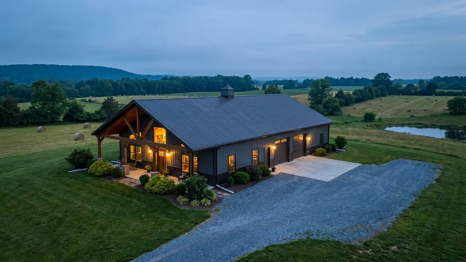 A finished barndominium at dusk with warm interior lighting glowing through its large windows.
