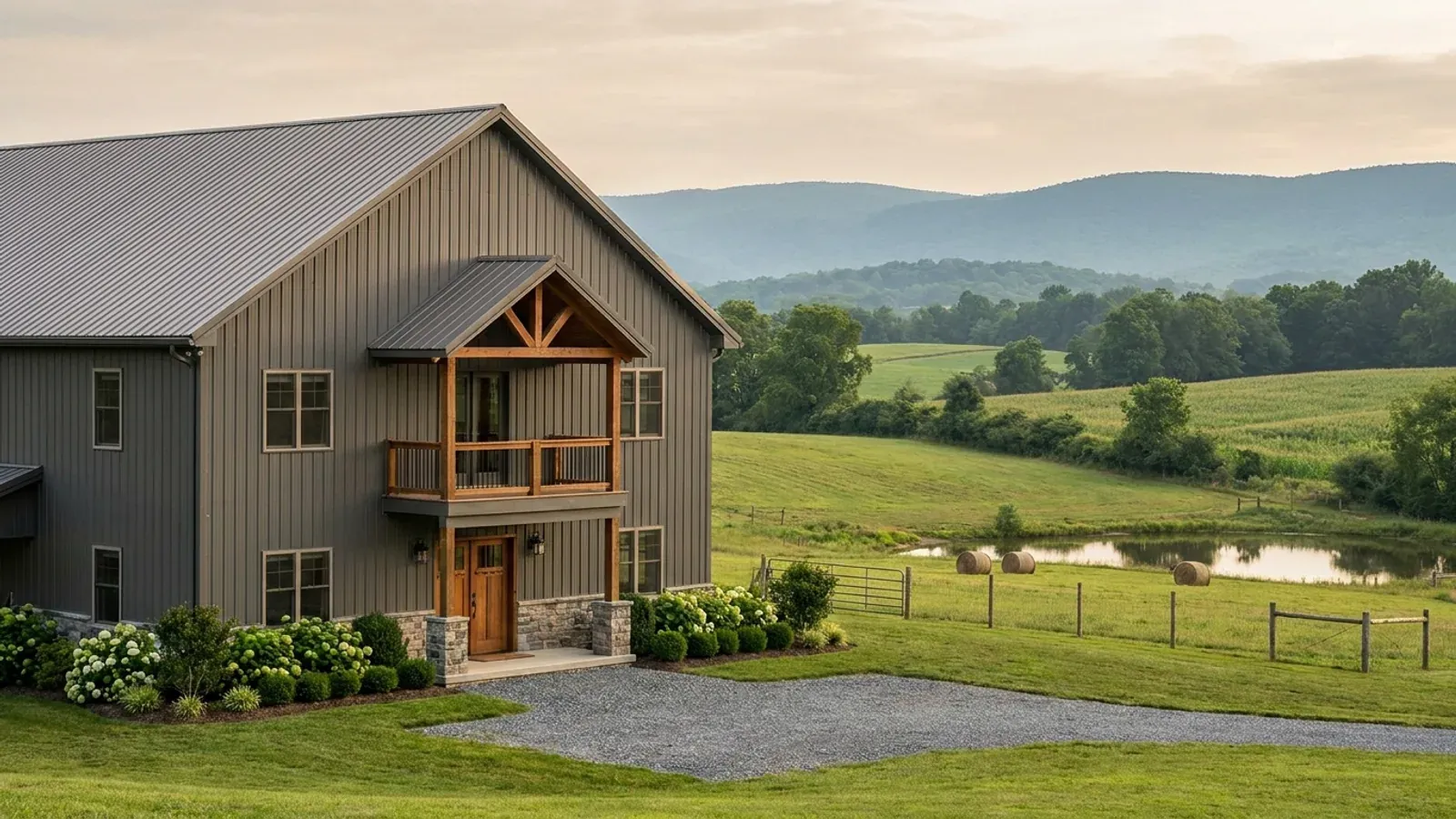 A completed two-story barndominium with visible second-story windows and a small covered balcony above the entry porch.